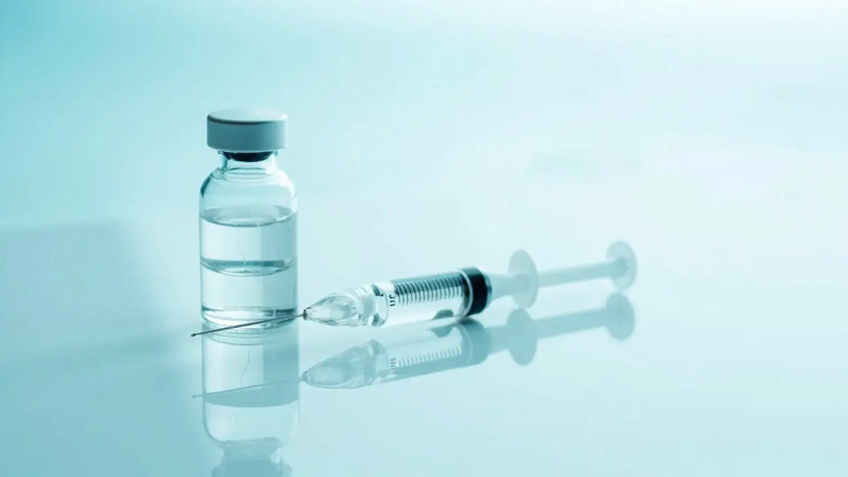 Clear glass vial of injectable peptide with gray cap next to syringe