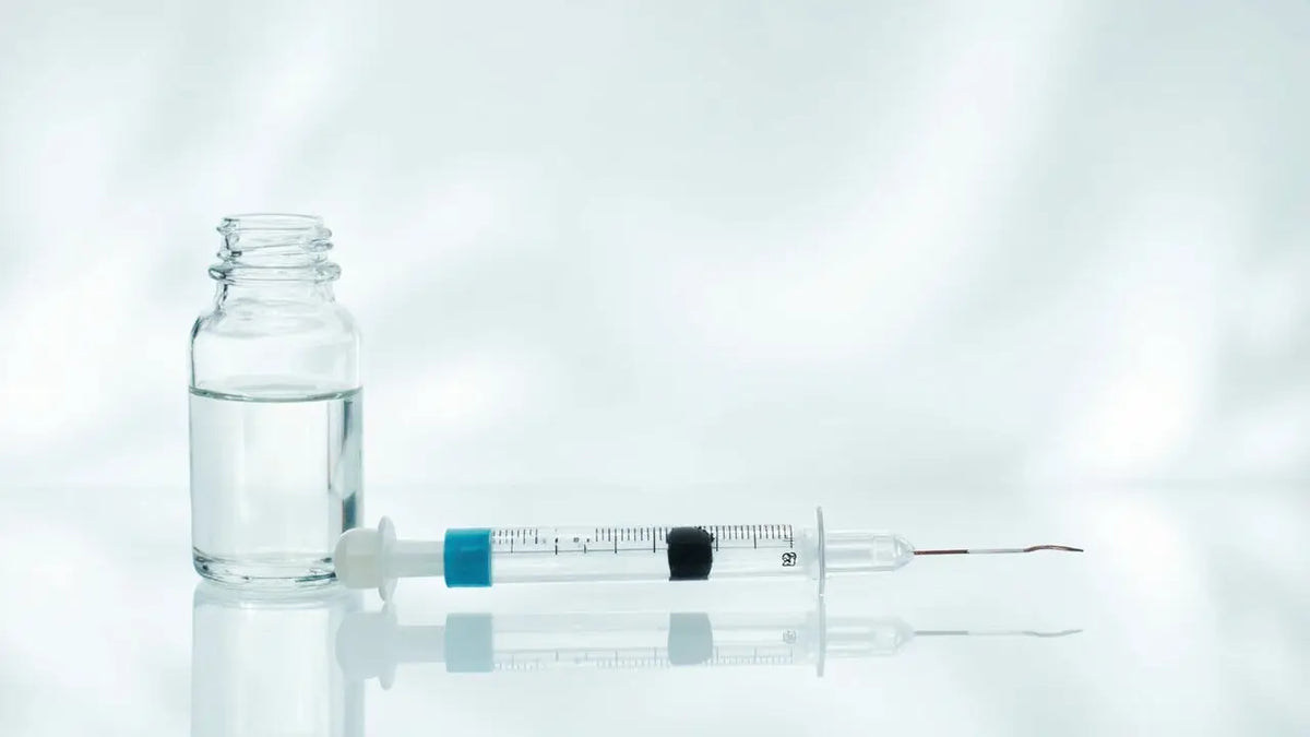 Clear glass vial with transparent liquid beside syringe with blue plunger and black needle cap for safe peptide injection at home