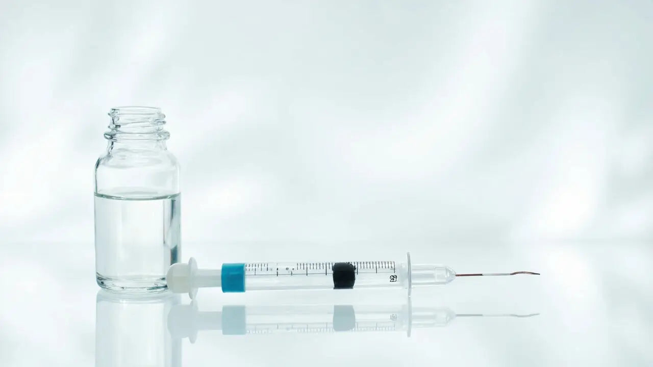 Clear glass vial with transparent liquid beside syringe with blue plunger and black needle cap for safe peptide injection at home