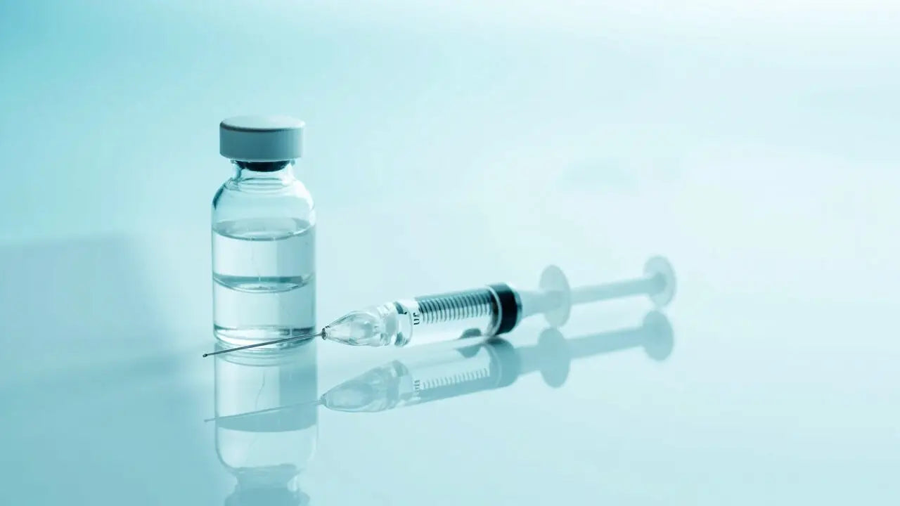 Clear glass vial of injectable peptide with gray cap next to syringe